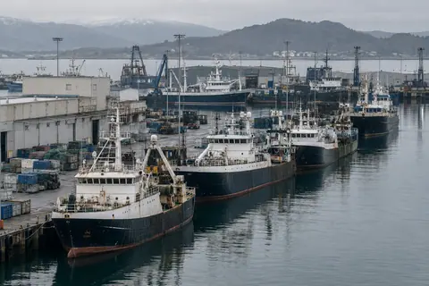 AI-generated illustration: Industrial fishing vessels lined up beside a large working harbor.